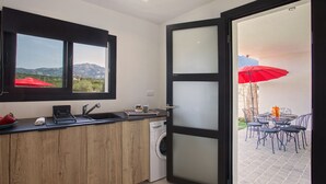Cocina compacta con lavadora, ventana con vistas a montañas y comedor con mobiliario de exterior.