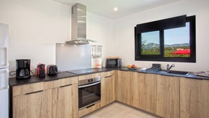 Una cocina moderna con armarios de madera, una campana extractora de acero inoxidable, horno empotrado, microondas y un ventanal con vistas panorámicas.