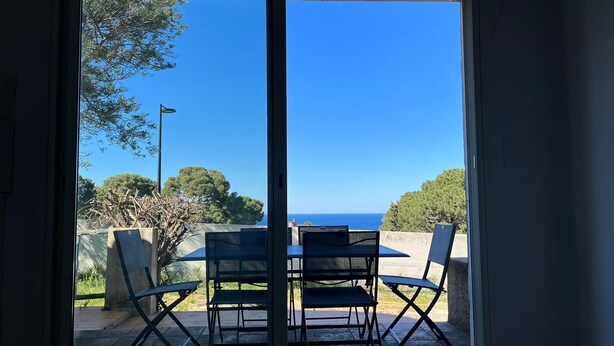 A room with a sliding glass door leading to an outdoor patio with a table and chairs, overlooking a clear blue sky and a distant view of the sea. - Sea view villa (Corbara)