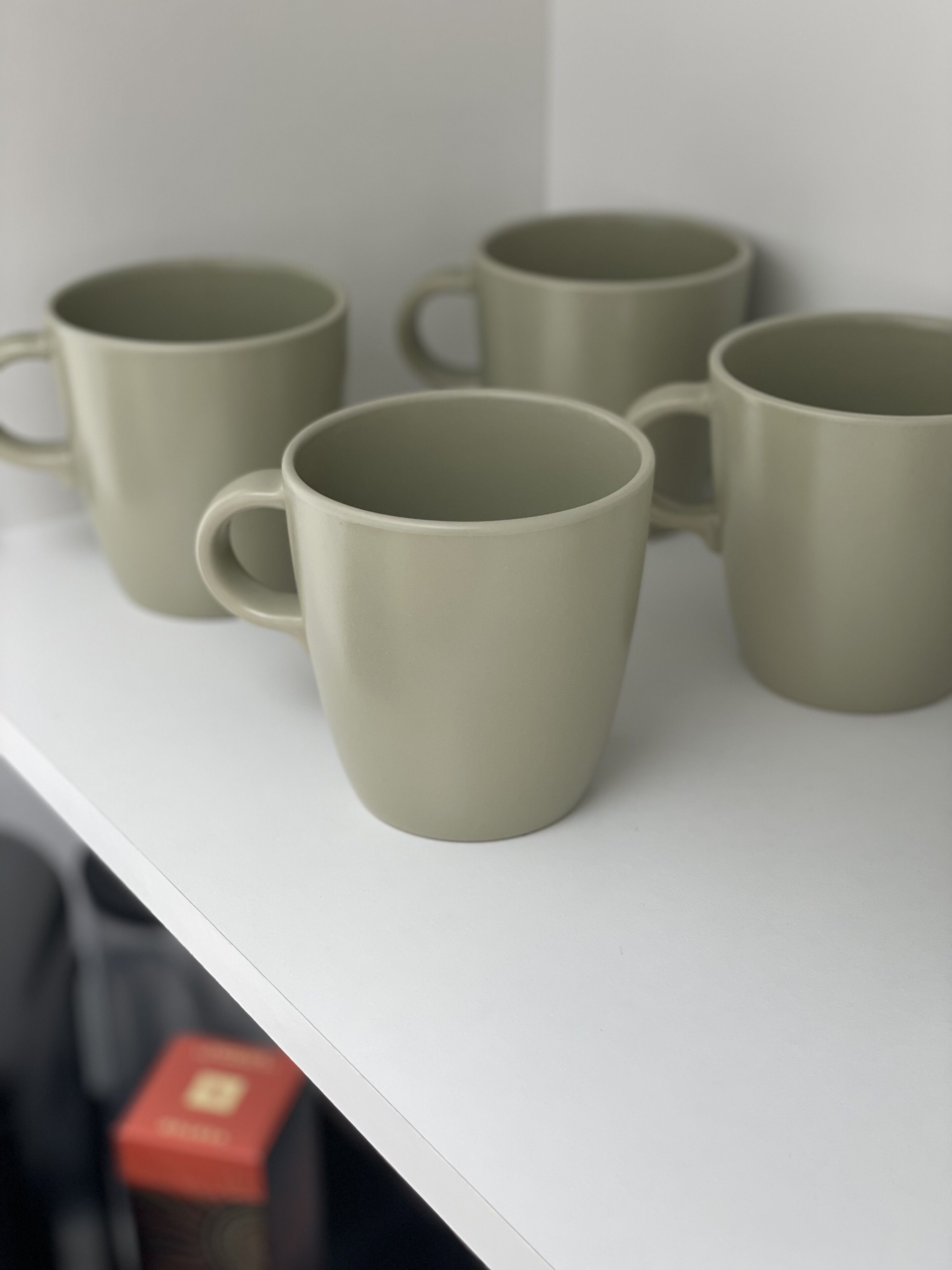 A set of four plain, matte-colored mugs on a white shelf.
