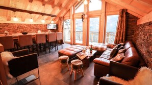 A cozy interior with a wooden ceiling, a stone wall, a leather sofa, and a dining area with chairs and a table. - Chalet, balcony, parking, tv, ski locker, 130m², Valloire (Valloire)