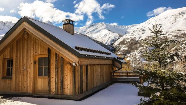 A wooden cabin with a snow-covered roof, set against a backdrop of snow-capped mountains and a clear sky. - Chalet, balcony, parking, tv, ski locker, 130m², Valloire (Valloire)