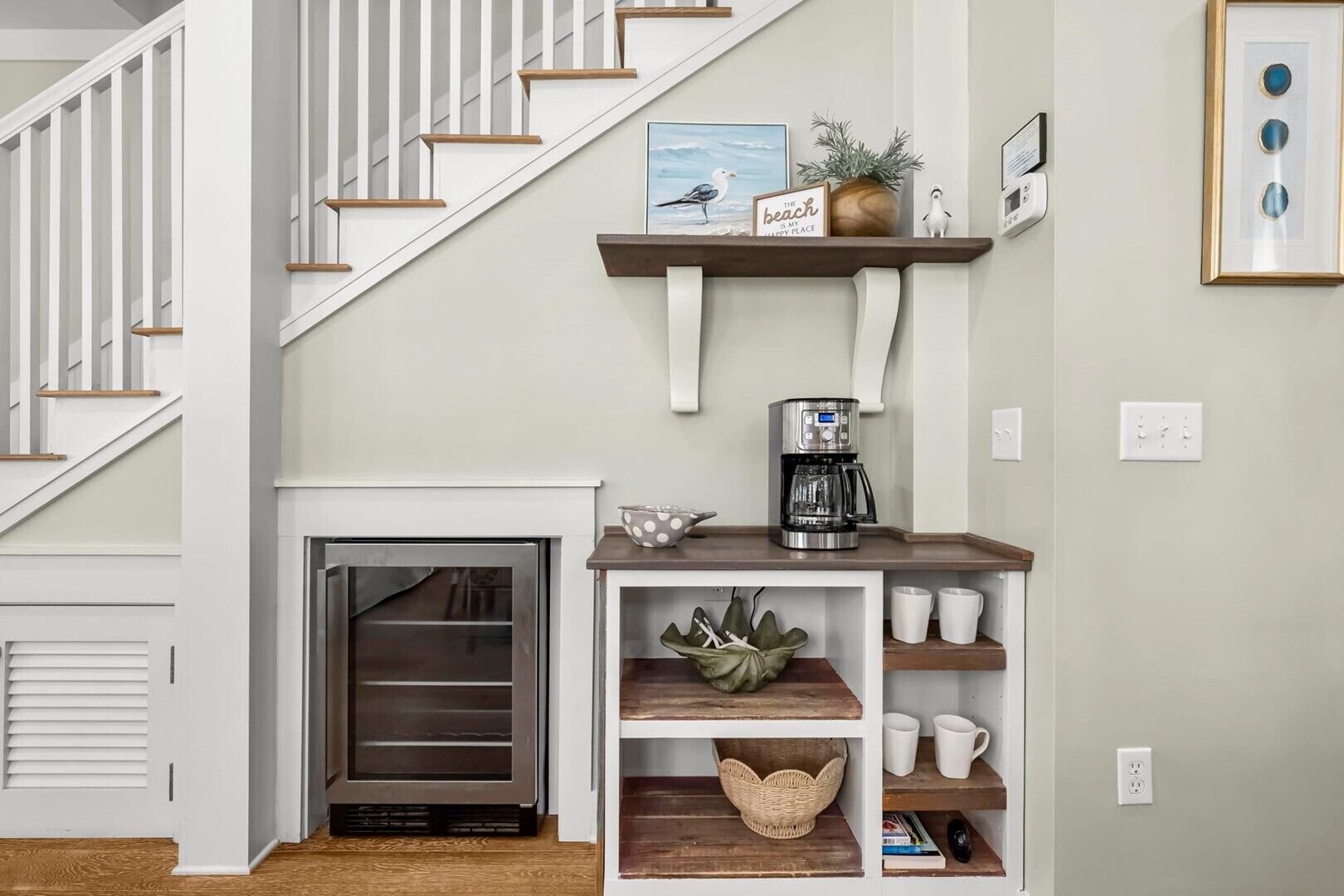 A staircase with white railings and wooden steps, a small fireplace with a glass door, a coffee maker on a wooden shelf, and a wall-mounted light switch.