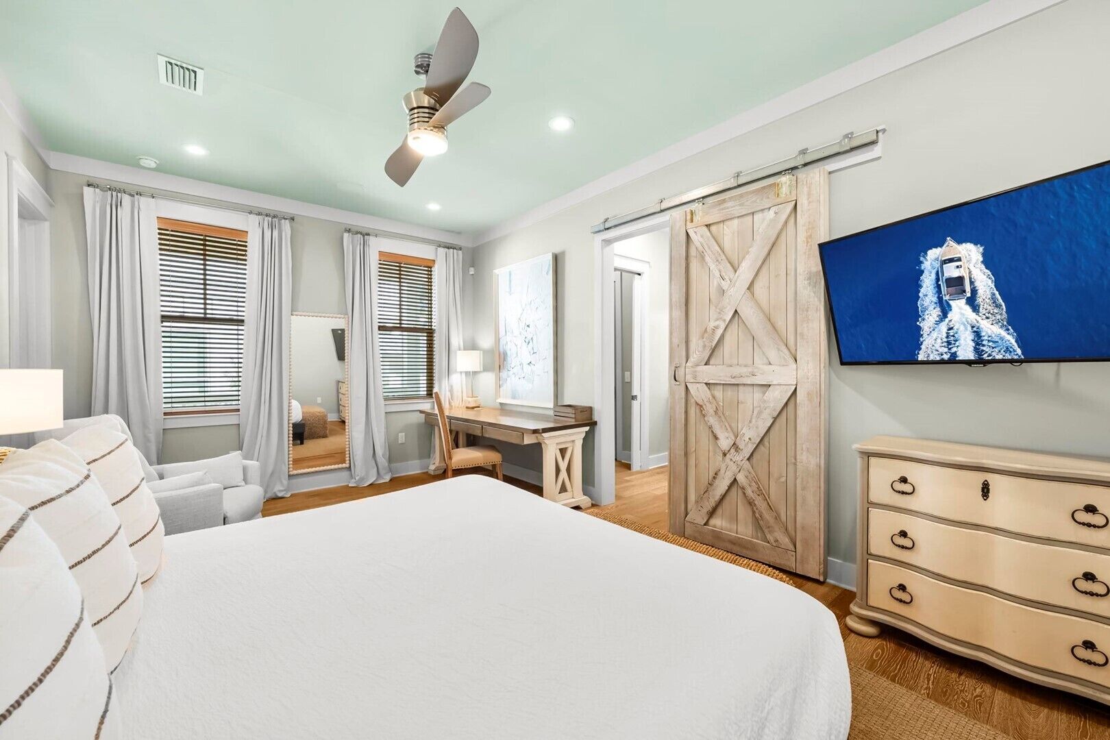 A bedroom with a large bed, a desk, a dresser, and a TV mounted on the wall.