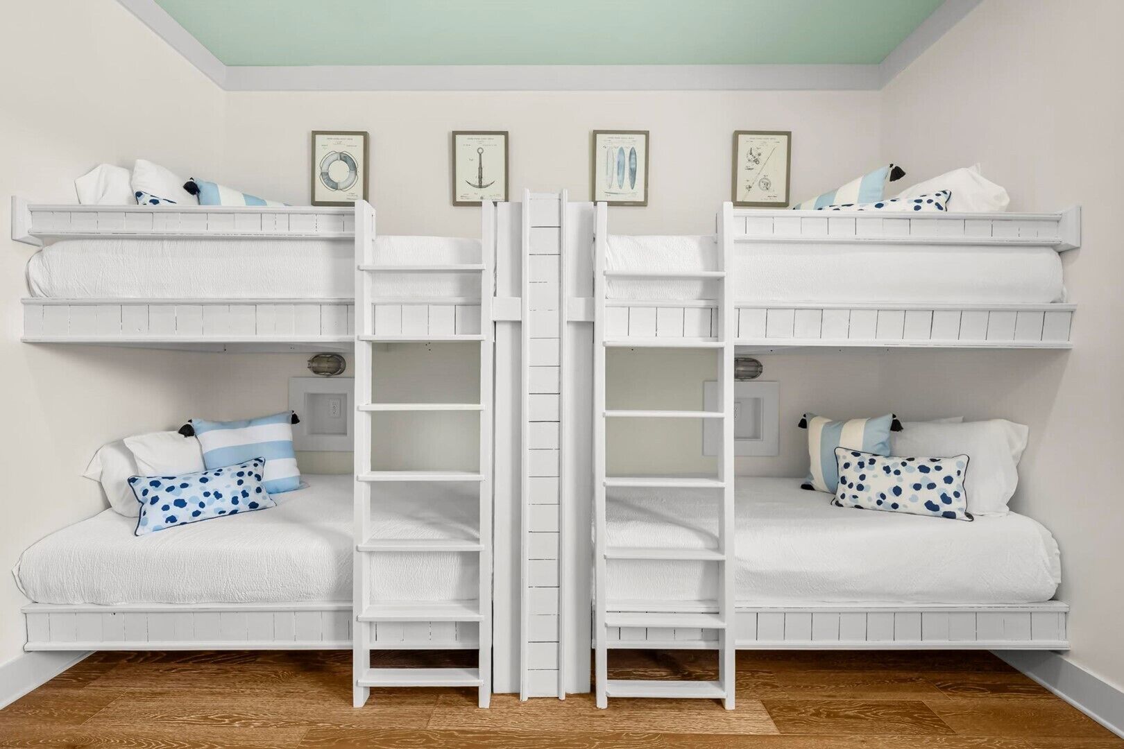 A bunk bed room with a ladder, white bedding, and nautical-themed wall art.