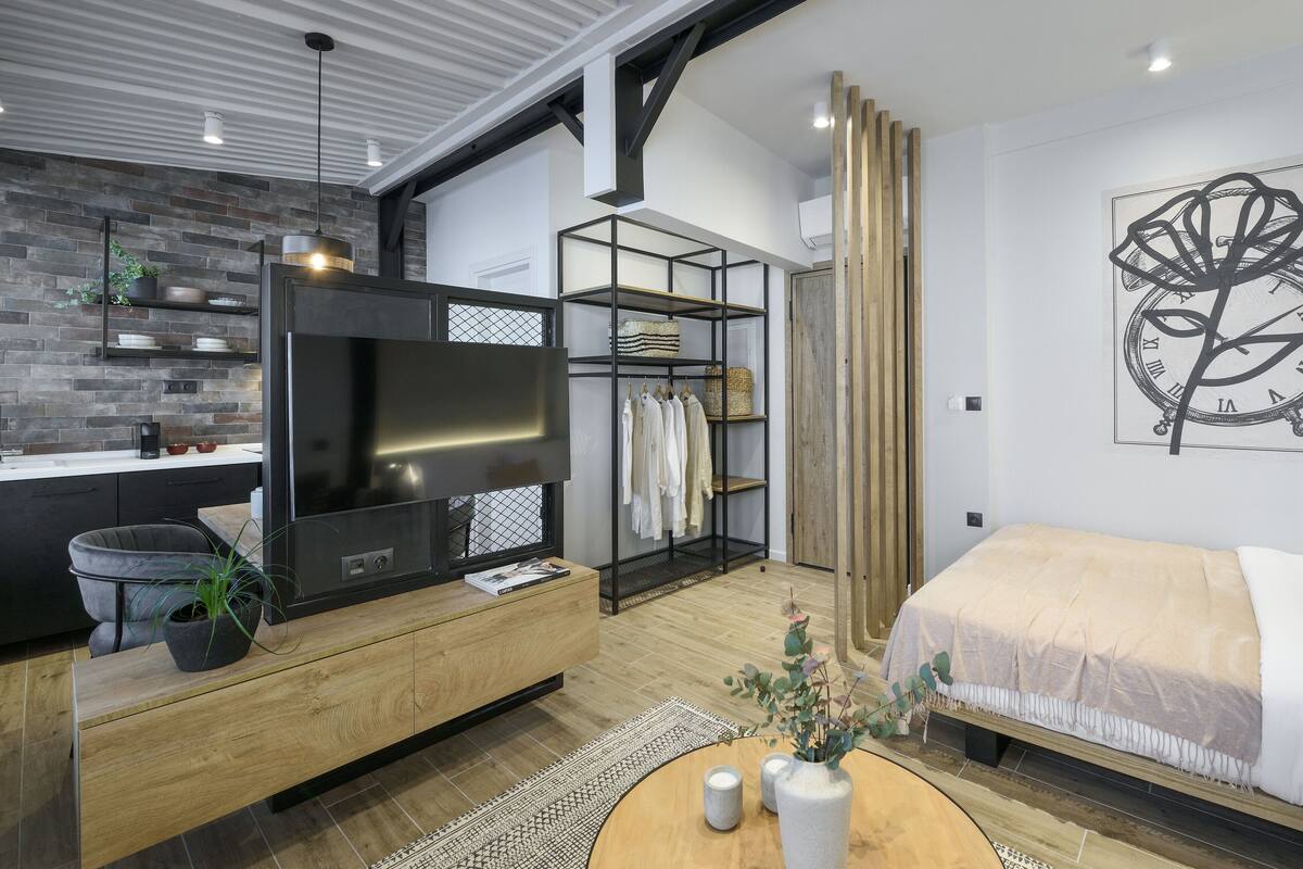 A modern bedroom with a large bed, a TV, a wardrobe, and a wall clock.