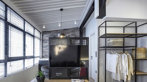 A modern living room with a flat-screen TV, wooden coffee table, and a clothing rack with white garments. - Olvios Lofts Ladadika (Thessaloniki)