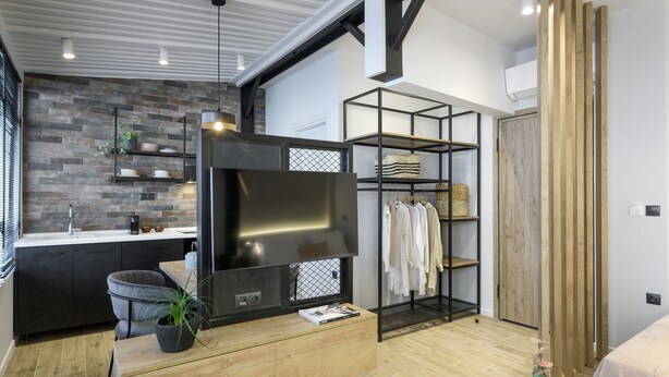A modern living room with a TV, wooden furniture, a brick wall, and a clothing rack. - Olvios Lofts Ladadika (Thessaloniki)