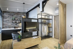 Un salon moderne avec un téléviseur, des meubles en bois, un mur en briques et un portant à vêtements.