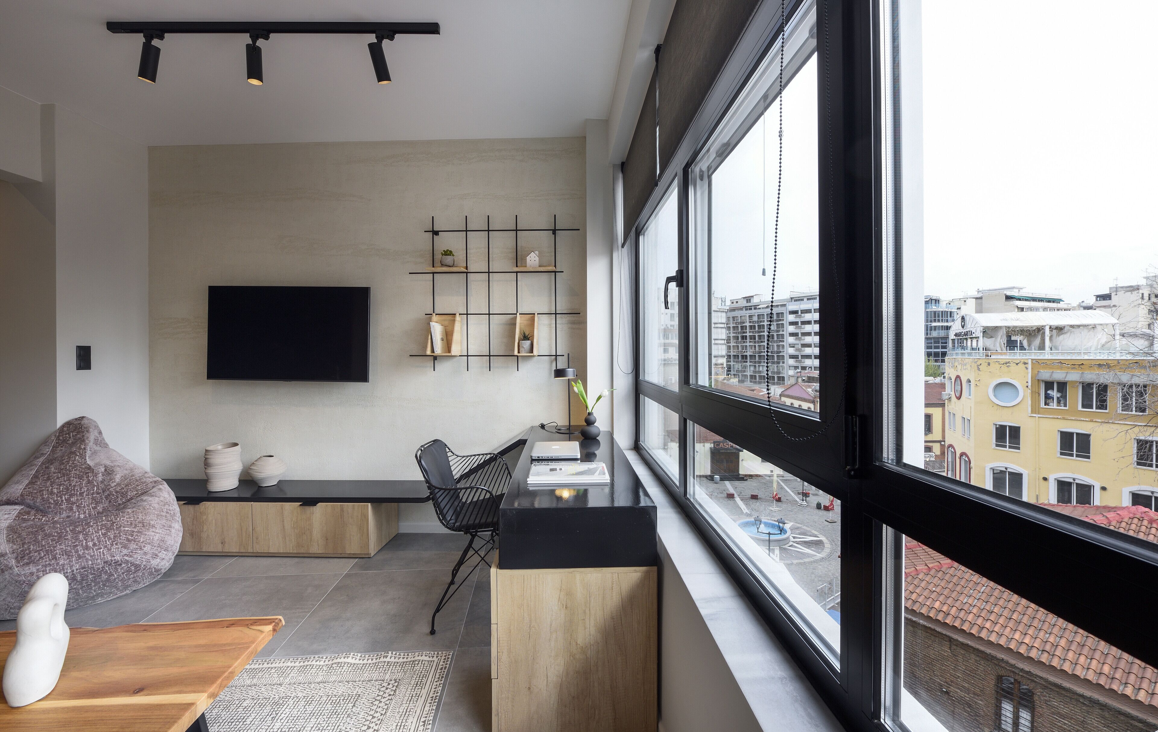 A modern living room with a large window, a flat-screen TV, a wooden coffee table, a bean bag, and a bookshelf.