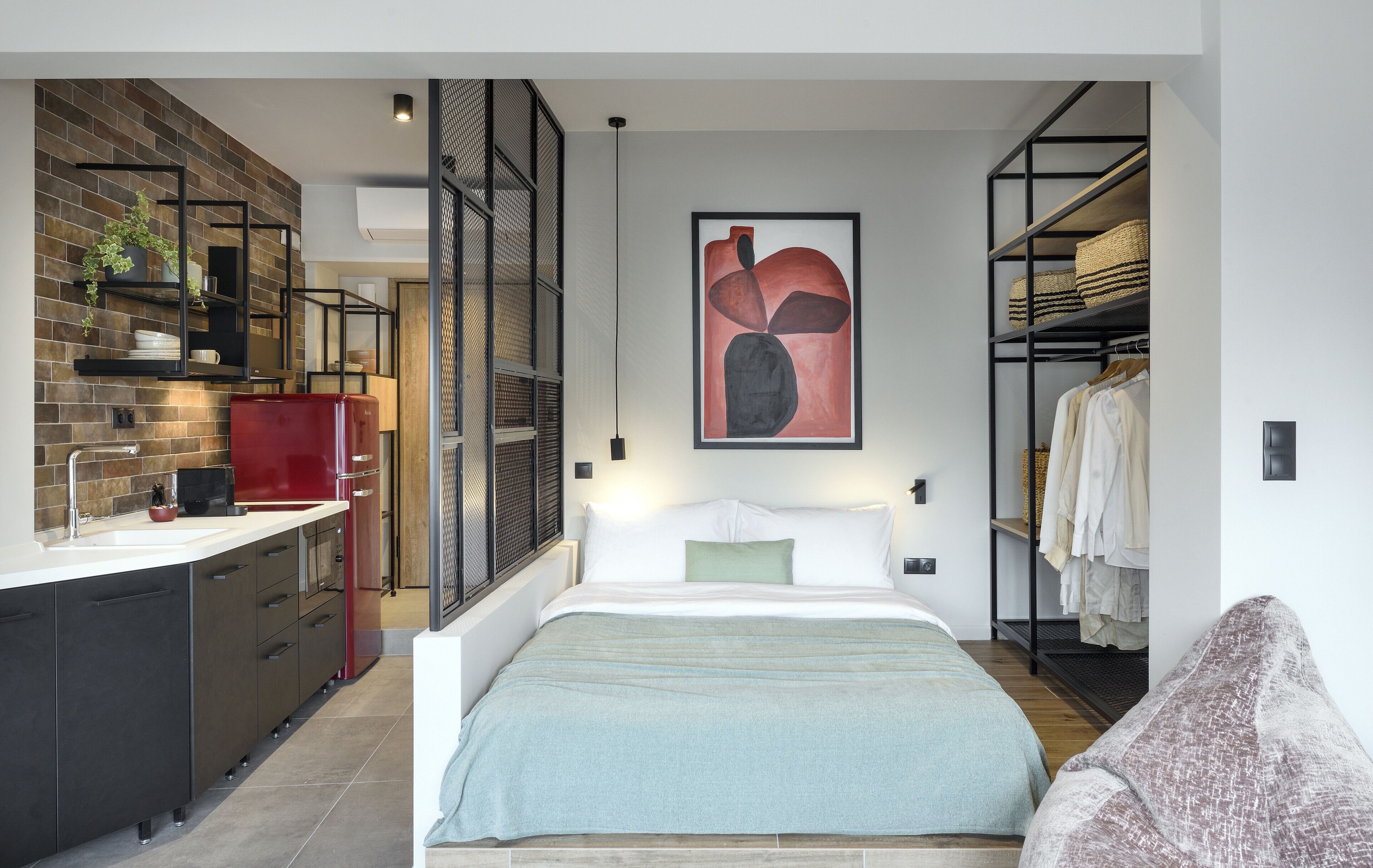 A modern bedroom with a large bed, a built-in wardrobe, and a kitchen area with a red refrigerator.
