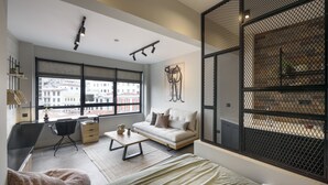 A modern living room with a sofa, a coffee table, a desk, and a large window with a city view. - Olvios Lofts Ladadika (Thessaloniki)