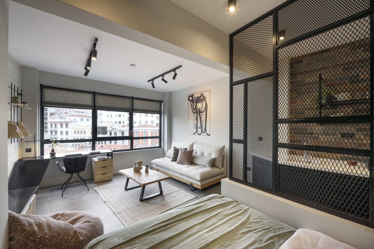 A modern living room with a sofa, a coffee table, a desk, and a large window with a city view.