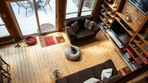 Ein gemütliches Wohnzimmer mit einer braunen Couch, zwei Tierbetten, einem Fernseher und einem Bücherregal.