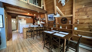 Ein rustikaler Innenraum aus Holz mit Küchenzeile, Esstisch und Stühlen.