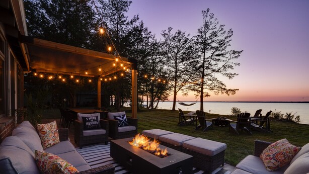 Een terras buiten met vuurkorf, rieten meubels en sfeerverlichting.