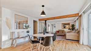 Een ruime woonkamer met een ronde eettafel, zwarte stoelen en een houten bank. Achterin is een grote spiegel en een bankstel zichtbaar.