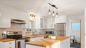 Een moderne keuken met witte kasten, roestvrijstalen apparatuur, een houten kookeiland en hanglampen.