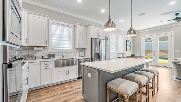A modern kitchen with white cabinetry, a central island with bar stools, stainless steel appliances, and pendant lighting. - 30A Beach House - Beach Ready By Panhandle Getaways (Panama City Beach)