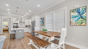 A modern kitchen with white cabinetry, a wooden dining table, and a bench. - 30A Beach House - Beach Ready By Panhandle Getaways (Panama City Beach)
