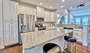 Una cocina moderna con armarios blancos, electrodomésticos de acero inoxidable, encimeras de granito y un taburete de bar.