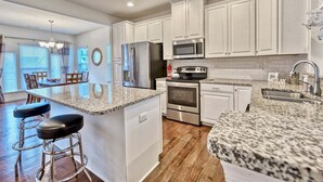 A kitchen with white cabinets, granite countertops, stainless steel appliances, and a bar area with stools.