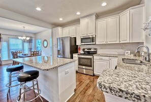A kitchen with white cabinets, granite countertops, stainless steel appliances, and a bar area with stools.