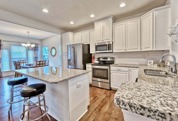 A kitchen with white cabinets, granite countertops, stainless steel appliances, and a bar area with stools.