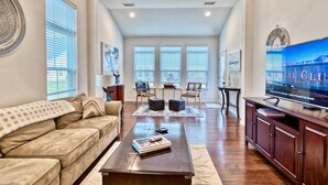 A spacious living room with a sofa, coffee table, TV, and a view of the outside through large windows.