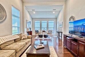 A spacious living room with a sofa, coffee table, TV, and a view of the outside through large windows.