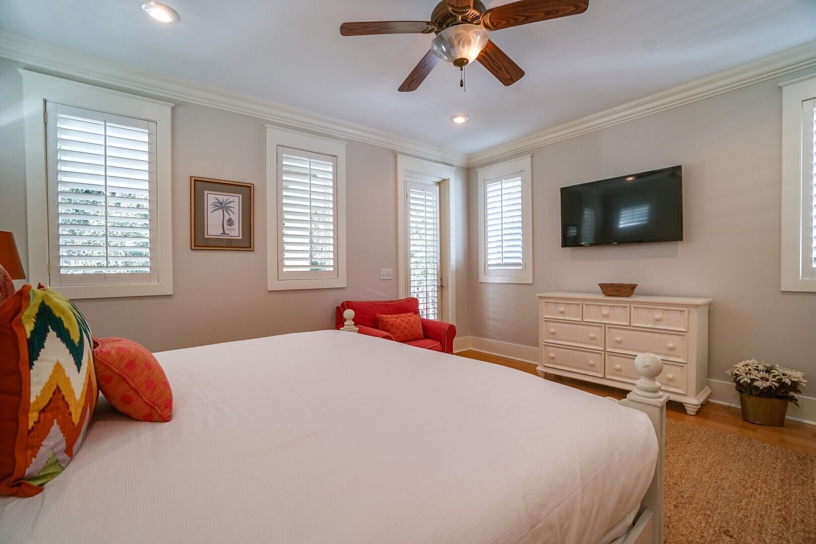 A bedroom with a large bed, a ceiling fan, a TV, and a dresser.