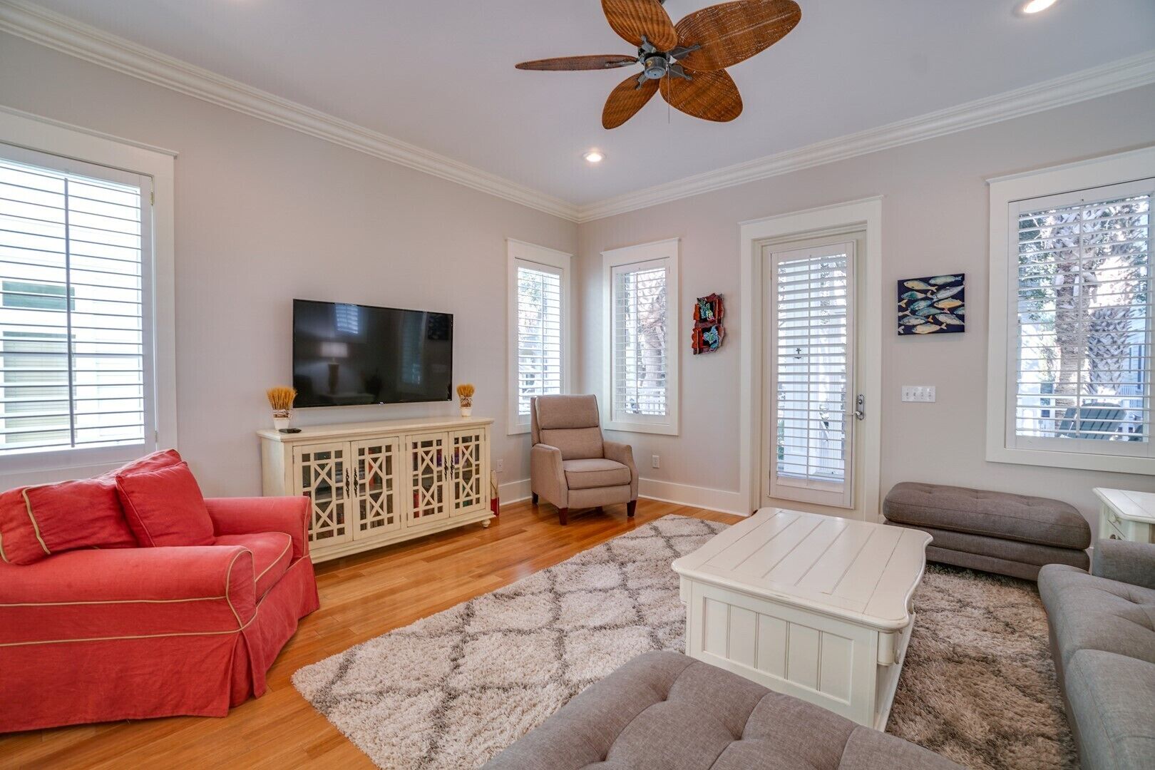 Un salon avec un téléviseur, un canapé rouge, un fauteuil beige, une table basse blanche et un ventilateur de plafond.