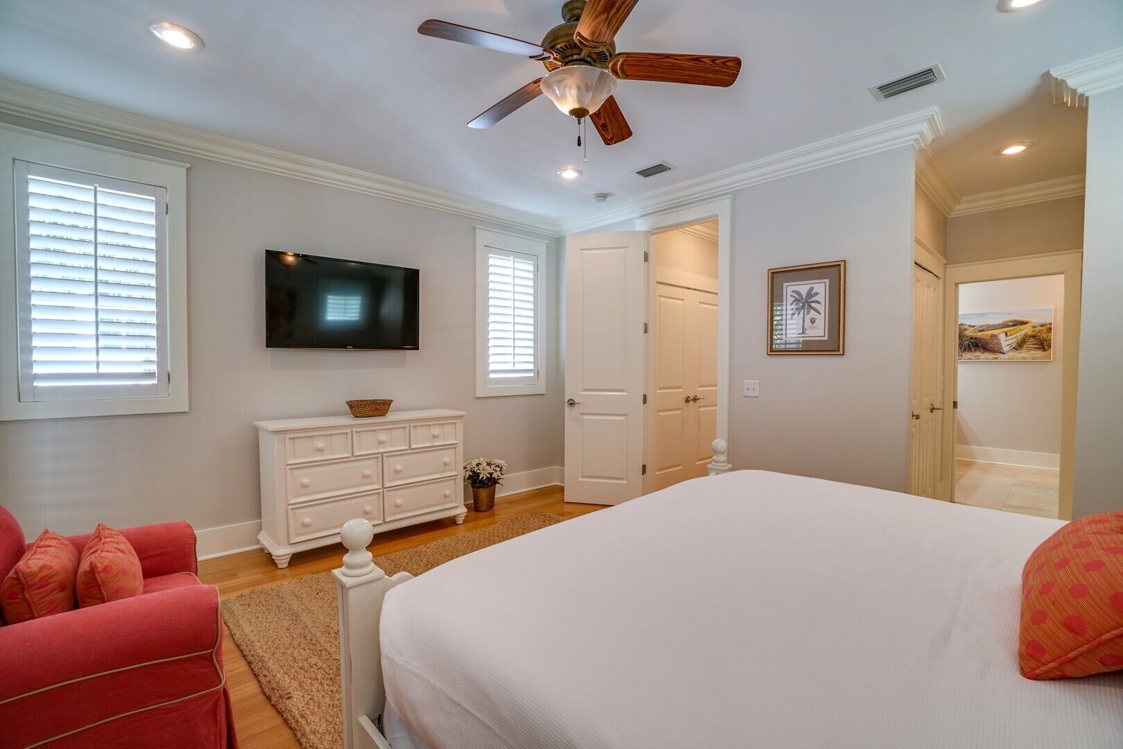 A bedroom with a bed, a ceiling fan, a TV, a dresser, and a door leading to another room.