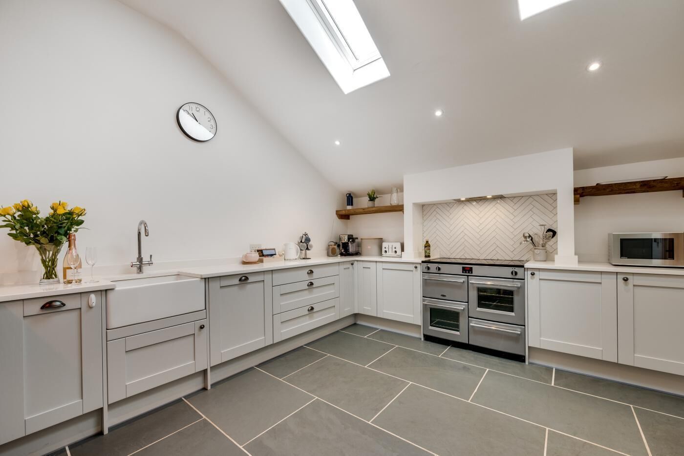 A modern kitchen with white cabinetry, a herringbone-patterned backsplash, a built-in oven, and a microwave.