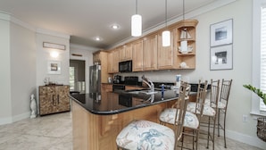 A kitchen with wooden cabinets, a black countertop, and a central island with bar stools. - 30A Beach House - Mar Chiquita By Panhandle Getaways (Panama City Beach)