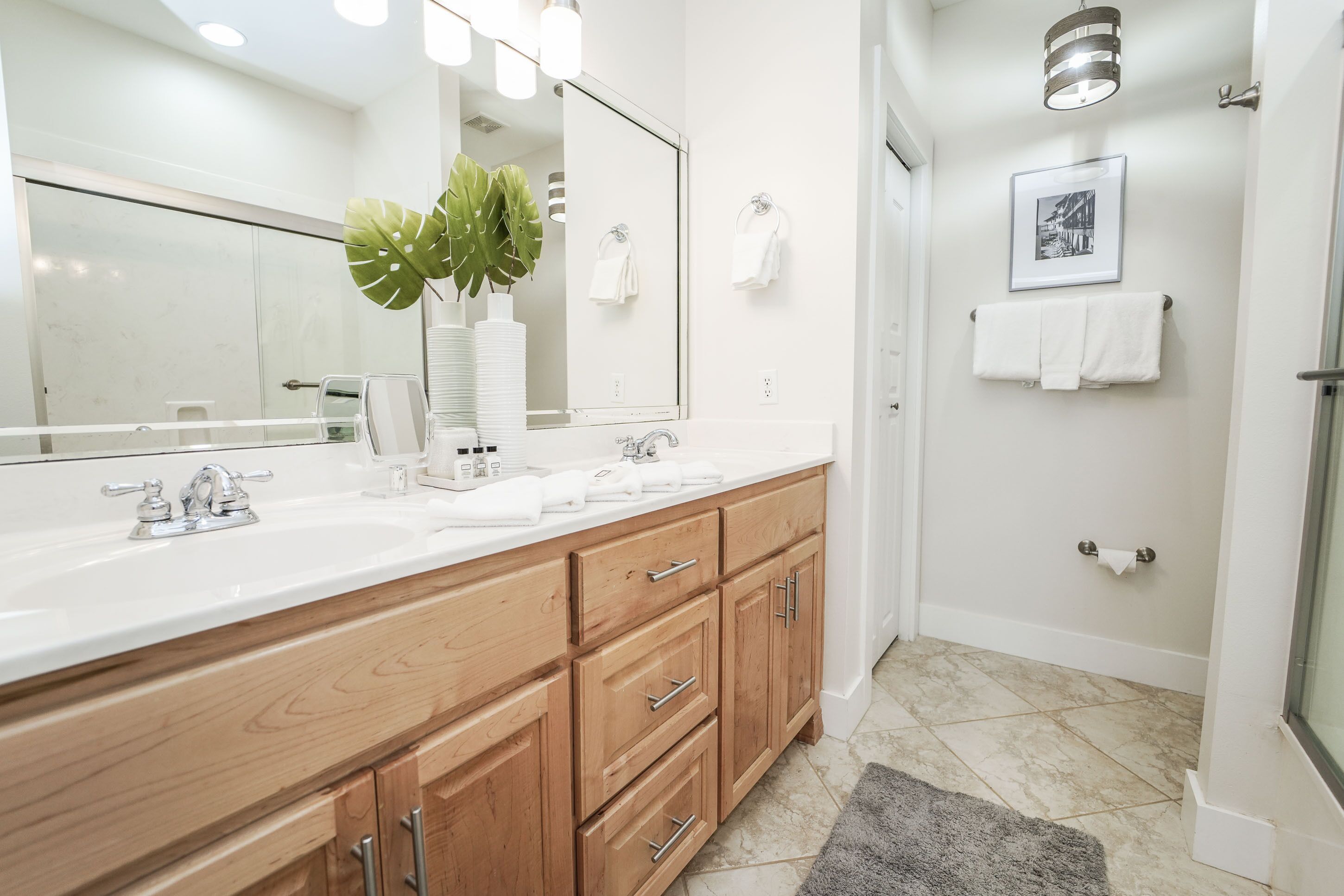 A modern bathroom with a white vanity, wooden cabinets, a large mirror, and a potted plant.