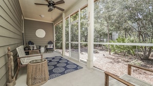 A covered porch with wicker furniture, a ceiling fan, and large windows overlooking a garden. - 30A Beach House - Mar Chiquita By Panhandle Getaways (Panama City Beach)