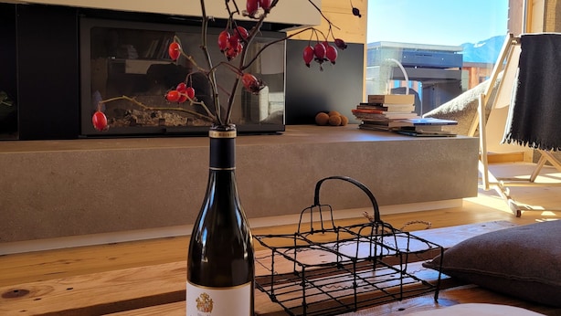 A bottle of wine on a wooden table with a view of mountains through a window. - Magnificent architect-designed chalet, breathtaking view of Mont Blanc (Hauteluce)