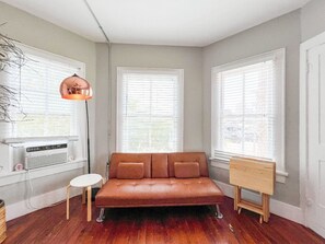 Ein Zimmer mit einer braunen Ledersofa, einem kleinen weißen Tisch und einer Staffelei aus Holz.