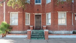 Un bâtiment en briques rouges, avec une porte d’entrée en bois, portant le numéro 308, et un petit escalier menant à l’entrée.