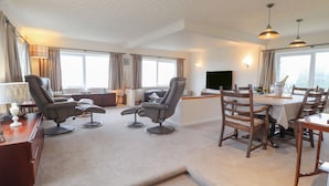 A spacious living area with a sofa set, a dining table with chairs, a TV, and a view of the outdoors. - Aelwyd Y Don (Cardigan)