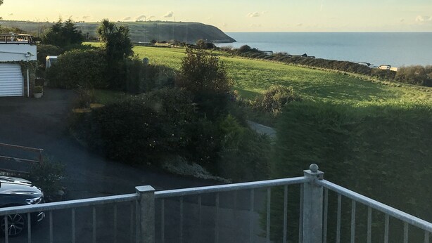 A coastal landscape with a grassy field, a road, and a building with a garage. - Aelwyd Y Don (Cardigan)