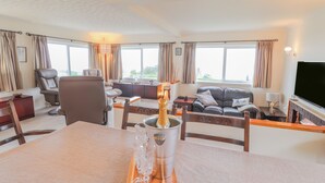 A spacious living room with a dining area, large windows, a fireplace, and a flat-screen TV. - Aelwyd Y Don (Cardigan)