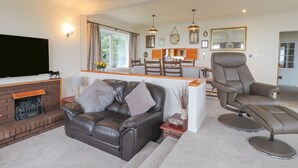 A modern living room with a leather sofa, a flat-screen TV, a fireplace, and a dining area with wooden furniture. - Aelwyd Y Don (Cardigan)