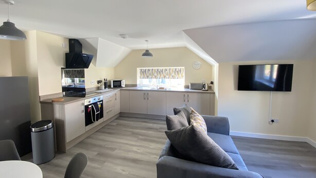 Een moderne keuken met een eethoek, een televisie aan de muur en een gezellige zithoek met een bank en kussens.