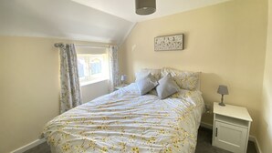 Een slaapkamer met een bed, nachtkastje, lamp, raam met gordijnen en een plafondlamp.