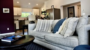 A modern living room with a grey sofa, a coffee table, and a book titled "A Day in the Life of America". - Renovated Modern Gem w/AC – Walk to Cooperstown All-Star Village, Sleeps 6 (Oneonta)