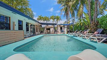 Relax by the pool surrounded by lush vegetation and palm trees, with lounge chairs and a covered patio for shade.