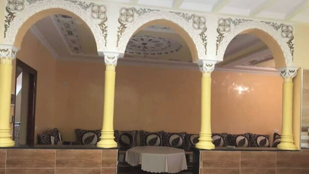A room with a tiled floor, a table with a white tablecloth, and a sofa with patterned cushions. - Family apartment in Tagadirte! (Agadir)