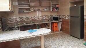 A kitchen with a granite countertop, a built-in microwave, a refrigerator, and a tiled backsplash. - Family apartment in Tagadirte! (Agadir)